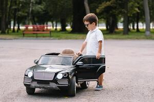 süß Junge im Reiten ein schwarz elektrisch Auto im das Park. komisch Junge Fahrten auf ein Spielzeug elektrisch Wagen. Kopieren Raum. foto