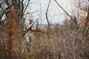 Jäger gut aussehend Kerl mit Waffe. Jäger verbringen Freizeit Jagd. Jagd Ausrüstung. brutal männlich Hobby. Mann beobachten Natur Hintergrund. Jäger halt Gewehr. Sicherheit Mittel. natürlich Umgebung foto