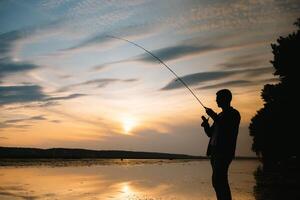 Fischer beim Sonnenuntergang auf das Fluss .Schön Sommer- Landschaft mit Sonnenuntergang auf das Fluss. Angeln. Spinnen beim Sonnenuntergang. Silhouette von ein Fischer. foto