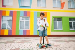 Junge geht zu Schule auf ein Roller. Kinder zurück zu Schule scoote.kinderschule Reiten ein Roller. zurück zu Schule. glücklich Kinder. glücklich Kindheit Lebensstil. Schüler geht zu Schule foto