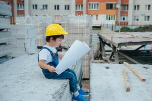 Architekt im Helm Schreiben etwas in der Nähe von Neu Gebäude. wenig süß Junge auf das Gebäude wie ein Architekt foto