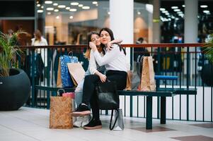 schön jung Mama und Teenager Tochter sind halten Einkaufen Taschen und lächelnd während tun Einkaufen im Einkaufszentrum. Familie Einkaufen foto