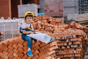 Architekt im Helm Schreiben etwas in der Nähe von Neu Gebäude. wenig süß Junge auf das Gebäude wie ein Architekt foto