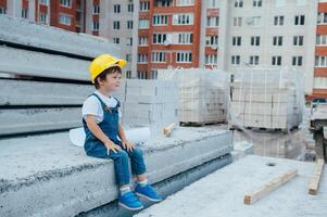 Architekt im Helm Schreiben etwas in der Nähe von Neu Gebäude. wenig süß Junge auf das Gebäude wie ein Architekt foto