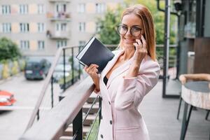 Geschäft Frau auf das Telefon beim Büro. jung Geschäft Frau haben Telefon Anruf beim das Büro. lächelnd Geschäft Frau. ziemlich jung Geschäft mit Smartphone beim das Dachgeschoss Büro. foto