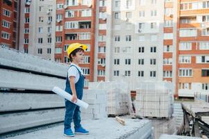 Architekt im Helm Schreiben etwas in der Nähe von Neu Gebäude. wenig süß Junge auf das Gebäude wie ein Architekt foto