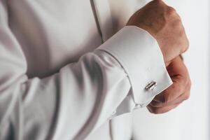 männlich Hände auf ein Hintergrund von ein Weiß Shirt, Ärmel Hemd mit Manschettenknöpfe und Uhren, fotografiert Nahansicht. foto