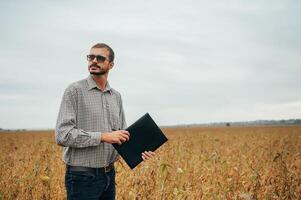 Agronom hält Tablette berühren Pad Computer im das Soja Feld und Prüfung Pflanzen Vor Ernte. Landwirtschaft Konzept. landwirtschaftlich Ingenieur Stehen im ein Soja Feld mit ein Tablette. foto