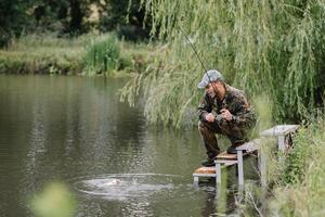 Fischer auf das Sommer- Hintergrund. Fischer im seine Hand halten Spinnen. Angeln, Spinnen Spule, Fisch, breg Flüsse. - - das Konzept von ein ländlich Flucht. Artikel Über Angeln foto