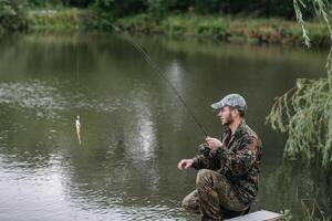 Angeln im Fluss.a Fischer mit ein Angeln Stange auf das Fluss Bank. Mann Fischer fängt ein Fisch Hechtangeln, Spinnen Spule, Fisch, breg Flüsse. - - das Konzept von ein ländlich Flucht. Artikel Über Angeln foto