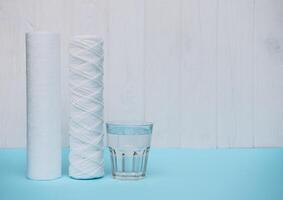 Wasser Filter. Kohlenstoff Patronen und ein Glas mit Wasser auf ein Blau Hintergrund. Haushalt Filtration System foto