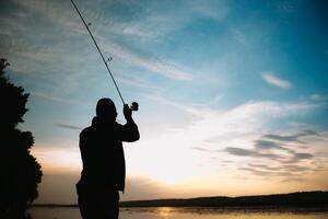 Angeln. Spinnen beim Sonnenuntergang. Silhouette von ein Fischer. foto