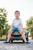 süß Junge im Reiten ein schwarz elektrisch Auto im das Park. komisch Junge Fahrten auf ein Spielzeug elektrisch Wagen. Kopieren Raum. foto