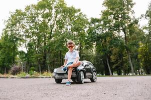 süß Junge im Reiten ein schwarz elektrisch Auto im das Park. komisch Junge Fahrten auf ein Spielzeug elektrisch Wagen. Kopieren Raum. foto