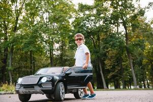 süß Junge im Reiten ein schwarz elektrisch Auto im das Park. komisch Junge Fahrten auf ein Spielzeug elektrisch Wagen. Kopieren Raum. foto