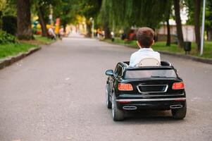 süß Junge im Reiten ein schwarz elektrisch Auto im das Park. komisch Junge Fahrten auf ein Spielzeug elektrisch Wagen. Kopieren Raum. foto