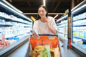 glücklich jung Frau suchen beim Produkt beim Lebensmittelgeschäft speichern. lächelnd Frau Einkaufen im Supermarkt foto