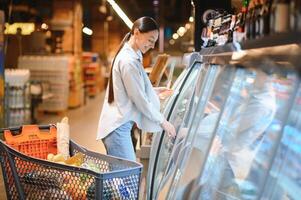 jung Frau mit ein Einkaufen Tasche wie ein Kunde Kauf Fisch beim das gekühlt Regal im das Supermarkt foto