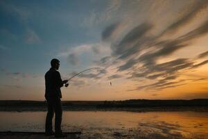 Fischer beim Sonnenuntergang auf das Fluss .Schön Sommer- Landschaft mit Sonnenuntergang auf das Fluss. Angeln. Spinnen beim Sonnenuntergang. Silhouette von ein Fischer. foto