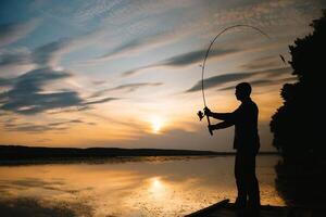 ein Fischer Silhouette Angeln beim Sonnenuntergang. frisches Wasser Angeln, Fang von Fisch. foto