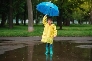 Kind spielen mit Spielzeug Boot im Pfütze. Kind abspielen draussen durch Regen. fallen regnerisch Wetter draußen Aktivität zum jung Kinder. Kind Springen im schlammig Pfützen. wasserdicht Jacke und Stiefel zum Baby. Kindheit foto