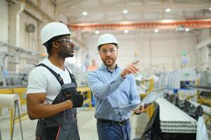 zwei vielfältig Fachmann schwer Industrie Ingenieure tragen Sicherheit Uniform und schwer Hüte Arbeiten auf Laptop foto