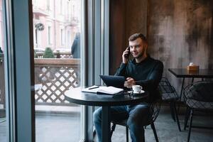 jung Geschäftsmann reden auf Handy, Mobiltelefon Telefon während Arbeiten auf Tablette im Cafe. foto