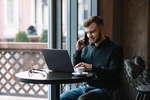 jung Geschäftsmann reden auf Handy, Mobiltelefon Telefon während Arbeiten auf Laptop im Cafe foto