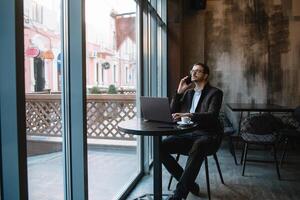 jung Geschäftsmann reden auf Handy, Mobiltelefon Telefon während Arbeiten auf Laptop im Cafe. foto