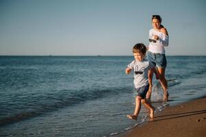 Mutter und Sohn spielen auf das Strand beim das Sonnenuntergang Zeit. Konzept von freundlich Familie. foto
