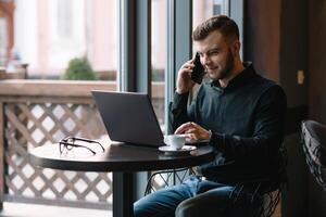 jung Geschäftsmann reden auf Handy, Mobiltelefon Telefon während Arbeiten auf Laptop im Cafe. foto