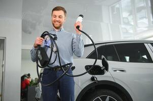 Bart Mann versuchen ein Neu Laden Kabel mit ein Auto Laden Bahnhof beim das Motor- Händler. Konzept von Kauf elektrisch Fahrzeug. Clever ökologisch Leben foto