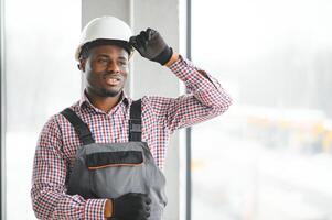 Porträt von gut aussehend afrikanisch Arbeiter oder Ingenieur im Overall und schwer Hut foto