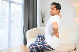 ein krank Mann auf Weihnachten hat stark zurück Schmerz, Massagen Muskel seine Hand Sitzung auf Sofa im Leben Zimmer foto