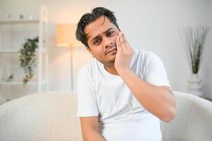 Zahnschmerzen Konzept. traurig ungesund indisch oder arabisch Kerl berühren Wange mit Hand mit schmerzlich Ausdruck foto