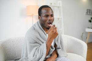 krank afrikanisch Mann mit Kehle sprühen beim Zuhause foto