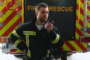 Feuerwehrmann im schützend Uniform Stehen in der Nähe von Feuer Motor auf Bahnhof foto