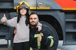 ein Feuerwehrmann nehmen ein wenig Kind Junge zu speichern ihn. Feuer Motor Auto auf Hintergrund foto