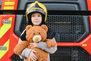 ein Junge tragen ein Feuerwehrmann Helm in der Nähe von ein Feuer LKW. foto