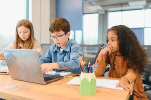 Porträt von Clever Schulmädchen und Schüler suchen beim das Laptop im Klassenzimmer foto