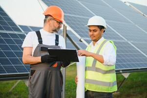 zwei männlich Ingenieure zur Zeit Arbeiten auf Pläne zu Installieren Solar- Paneele beim verlängerbar Solar- Leistung Pflanzen. Ingenieur Mannschaft Gespräche Über Installation Solar- Zellen auf ländlich Bereiche foto