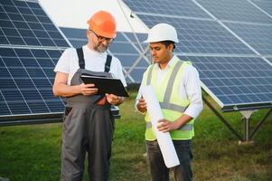 zwei männlich Ingenieure zur Zeit Arbeiten auf Pläne zu Installieren Solar- Paneele beim verlängerbar Solar- Leistung Pflanzen. Ingenieur Mannschaft Gespräche Über Installation Solar- Zellen auf ländlich Bereiche foto