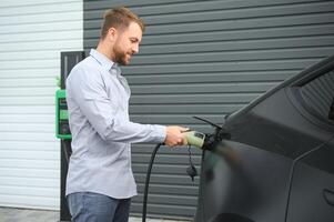 Mann halten Leistung Laden Kabel zum elektrisch Auto im draussen Auto Park foto