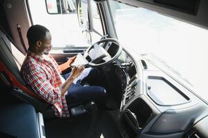 Fachmann afrikanisch amerikanisch LKW Treiber im beiläufig Kleider Fahren LKW Fahrzeug gehen zum ein lange Transport Route. foto
