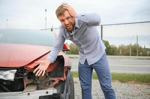 ein frustriert Mann in der Nähe von ein gebrochen Wagen. gepackt meine Kopf realisieren das Beschädigung ist ernst, das Auto ist darüber hinaus Reparatur foto