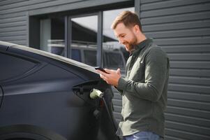 ein Mann Gebühren seine modern elektrisch Wagen. das Konzept von Grün Energie foto