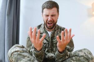 Nahansicht Porträt von emotional jung Militär- Mann schreiend und gestikulieren, Sitzung auf Couch beim Zuhause und Weinen. unzufrieden Soldat Besuch Psychologe, Leiden von posttraumatisch betonen, Kopieren Raum foto