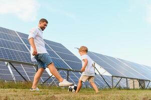 Vater und Sohn haben Spaß spielen Fußball in der Nähe von das Solar- Tafeln. das Konzept von Grün Energie foto