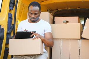 Porträt von ein jung afrikanisch amerikanisch Paket Lieferung Mann in der Nähe von ein Auto mit Boxen. foto