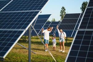 jung Familie von drei ist duckte sich in der Nähe von Photovoltaik Solar- Tafel, wenig Junge und Eltern. modern Familie Konzept. das Konzept von Grün Energie foto